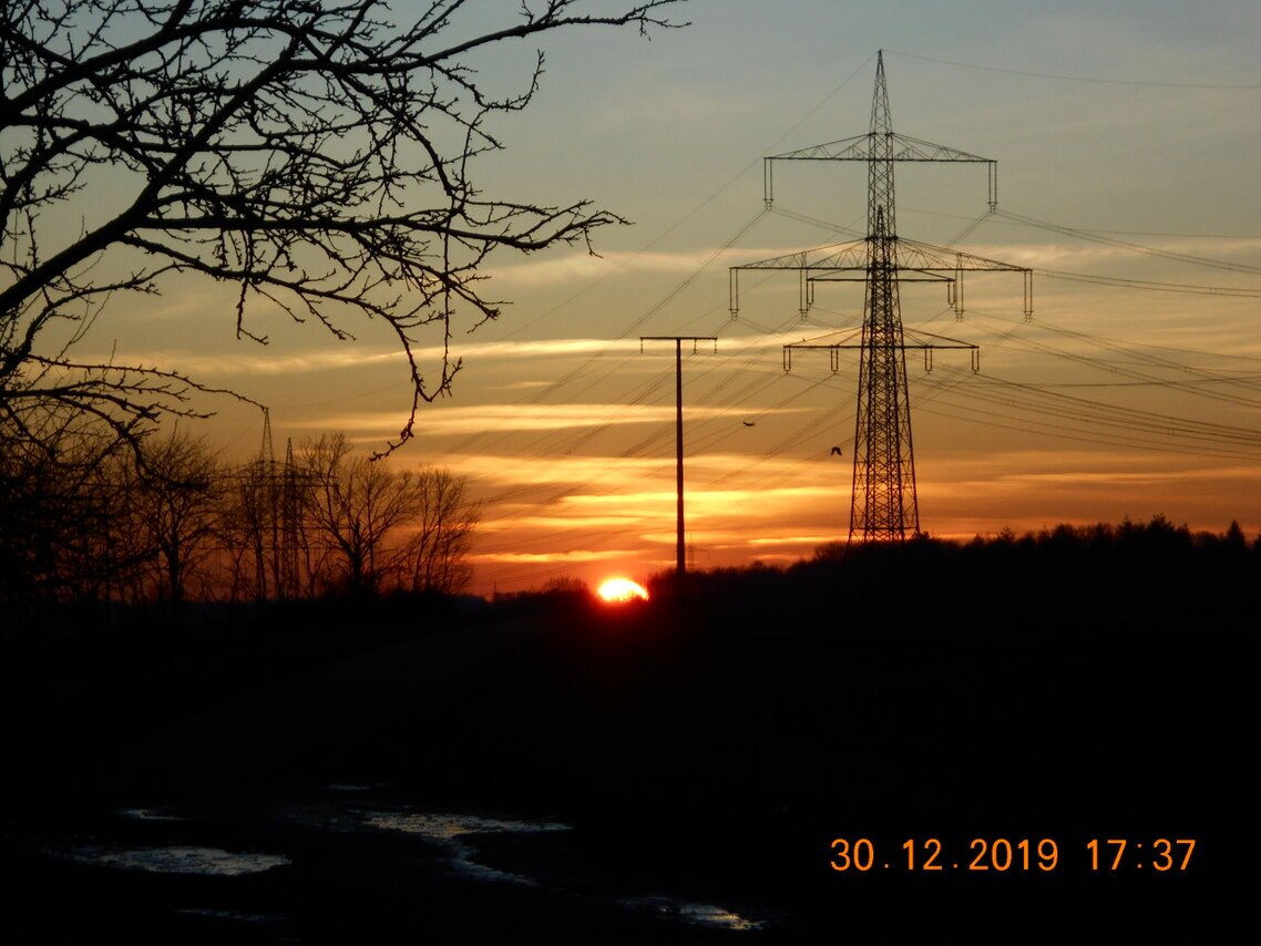 Sonne geht unter links vo zwei Strommasten im Dezember